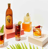 An artfully arranged display of 4 different cocktails set on bright colored boxes with palm fronds in the foreground. A bottle of Nixta prominently shown in the background. You're led to assume from the image that all these cocktails are made from Nixta, Licor de Elote.