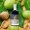 Nocino Walnut Liqueur bottle against a backdrop of fresh green walnuts and their leaves. A few ripe walnuts sit to the side.