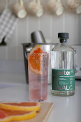 Bottle of Quarter Proof tequila with a cocktail and orange slices on a kitchen counter.