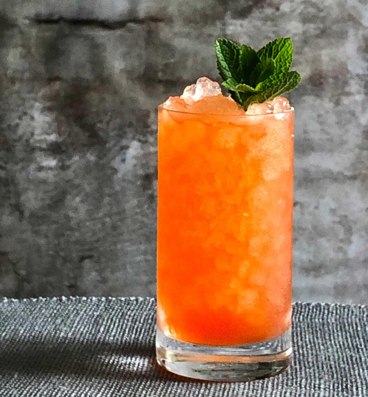 Orange cocktail with a mint leaf on a textured surface and background