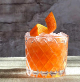 Orange cocktail with ice and orange slices in a textured glass against a stone wall background
