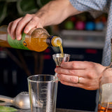 Person pouring liquid from a bottle into a cocktail shaker with a blurred background