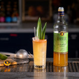 Cocktail with a garnish and bottle of Liber Pineapple Gum Syrup on a bar counter.