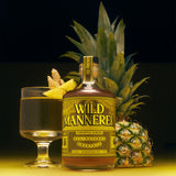 A bottle of Wild Mannered Pineapple Gingers All-Natural Cocktail centered between a filled coupe glass with a lemon twist and two whole pineapples on a black background with warm yellow lighting.