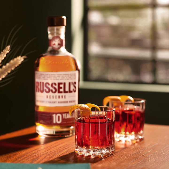 Russell's Reserve whiskey bottle with two cocktails on a wooden surface
