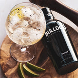Bottle of Bulldog London Dry gin with a cocktail and lime wedges on a wooden board