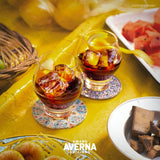 Two glasses of Amaro Averna with ice cubes on a yellow tablecloth, surrounded by fruits and cookies.
