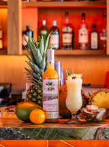 Tropical drink with a bottle of Chinola pineapple liqueur on a bar counter.