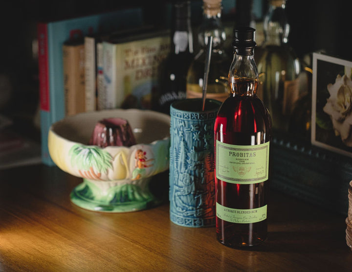 Bottle of Probitas Green Label Rum on a wooden surface with books and decorative items in the background