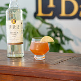 Liber tonic syrup bottle with a cocktail garnished with a lemon slice on a wooden surface.