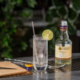 Cocktail with lime wheel and glass on a bar with Liber & Co Premium Tonic Syrup.