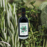 Bottle of Dansk Mjod Philosopher's Stone Viking Shrub Herb Edition over back drop of herbs.