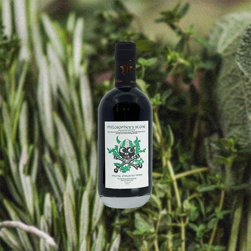 Bottle of Dansk Mjod Philosopher's Stone Viking Shrub Herb Edition over back drop of herbs.