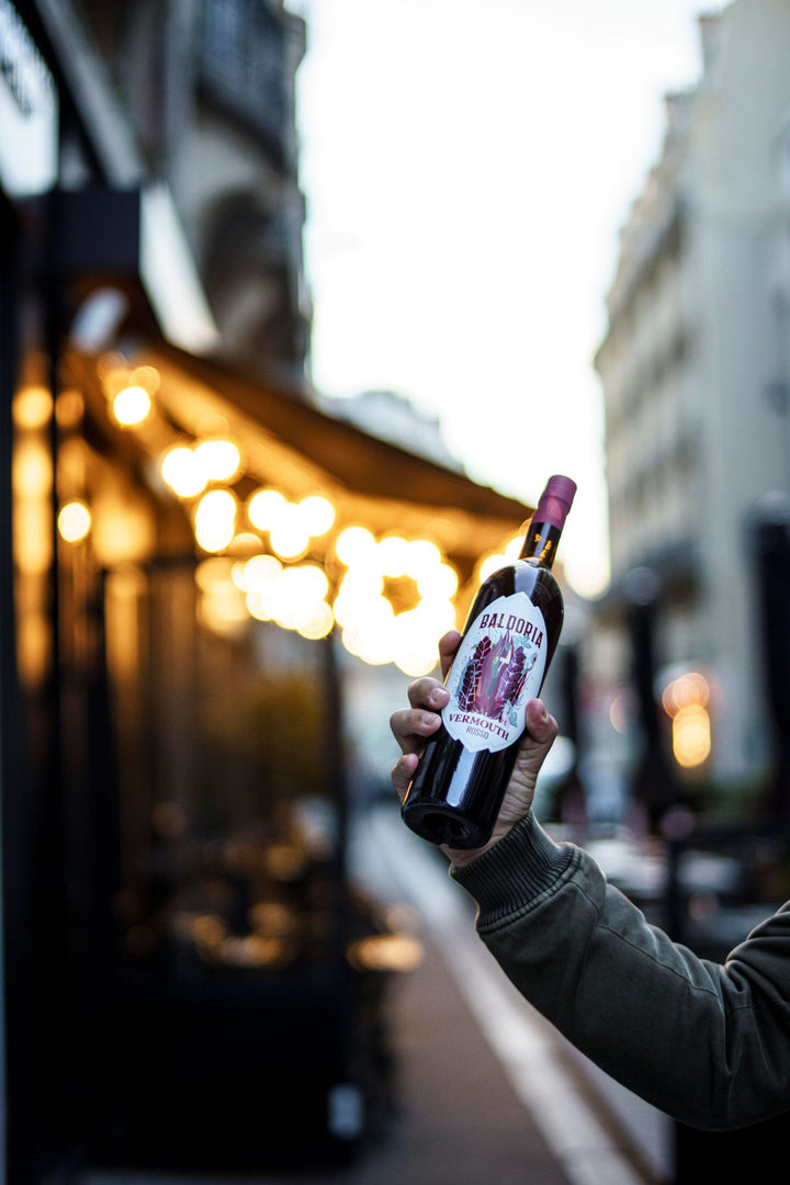 Person holding a bottle of Calvados in an urban setting with blurred lights and buildings.