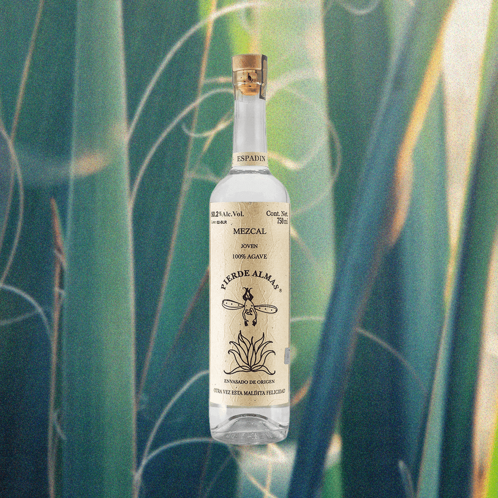 A tall thin bottle of mezcal with a craft paper label that reads: Mezcal Joven 100% Agave Pierde Almas. There is an simple illustration of a devil like character with wings diving blissfully into an agave plant.  This is set against a backdrop of a macro shot of agave plant at dusk, with a golden light shining on them.