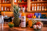 Bottle of Chinola pineapple liqueur on a bar counter with a pineapple and other fruits.