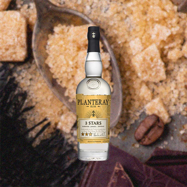 Bottle of Planteray 3 Stars White Jamaican Rum - formerly Plantation - against a backdrop of coard brown sugar, chocolate, and coffee beans.