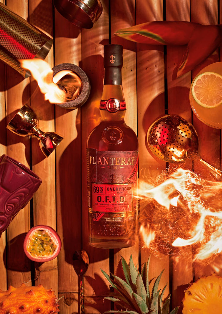Bottle of Planteray OFTD with flaming torch and tropical fruits on a wooden background