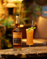 Bottle of Planteray rum next to a cocktail on a table with a blurred background