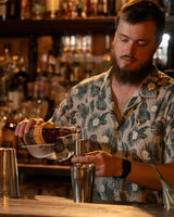 Man pouring a drink at a bar with bottles and glasses in the background
