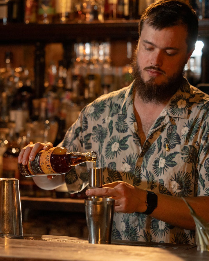 Man pouring a drink at a bar with bottles and glasses in the background