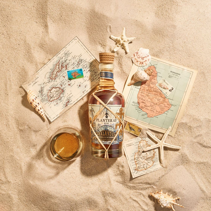 Bottle of Planters Manhattan whiskey on sand with maps and shells