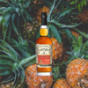 750ml bottle of Planteray Stiggins' Fancy Pineapple Rum - against a backdrop of fresh pineapples.