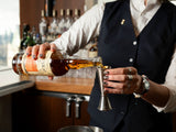 Bartender pouring liquid from a bottle into a jigger in a bar setting