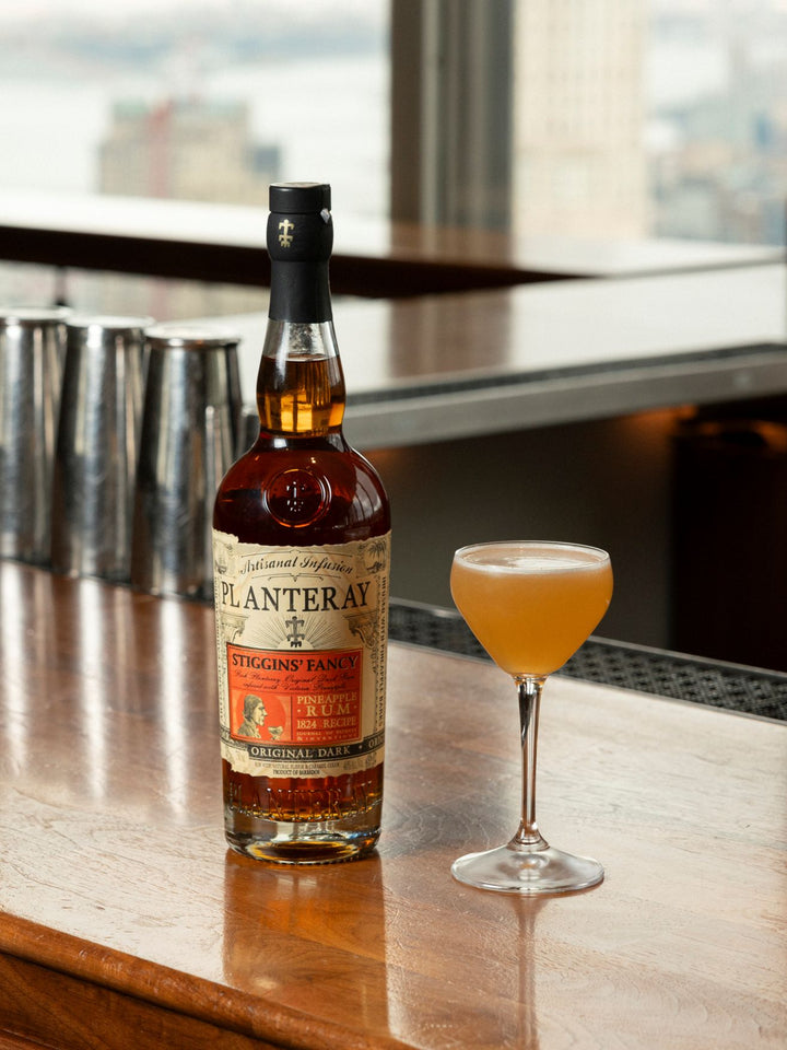 Bottle of Planteray Stiggin's Fancy Rum  on a bar with a glass of cocktail in the foreground