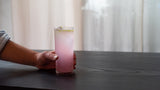 Hand holding a glass of pink drink on a table with a blurred background
