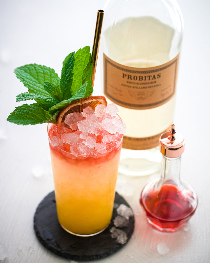Cocktail with ice and garnish next to a bottle labeled 'Probitas' on a white background