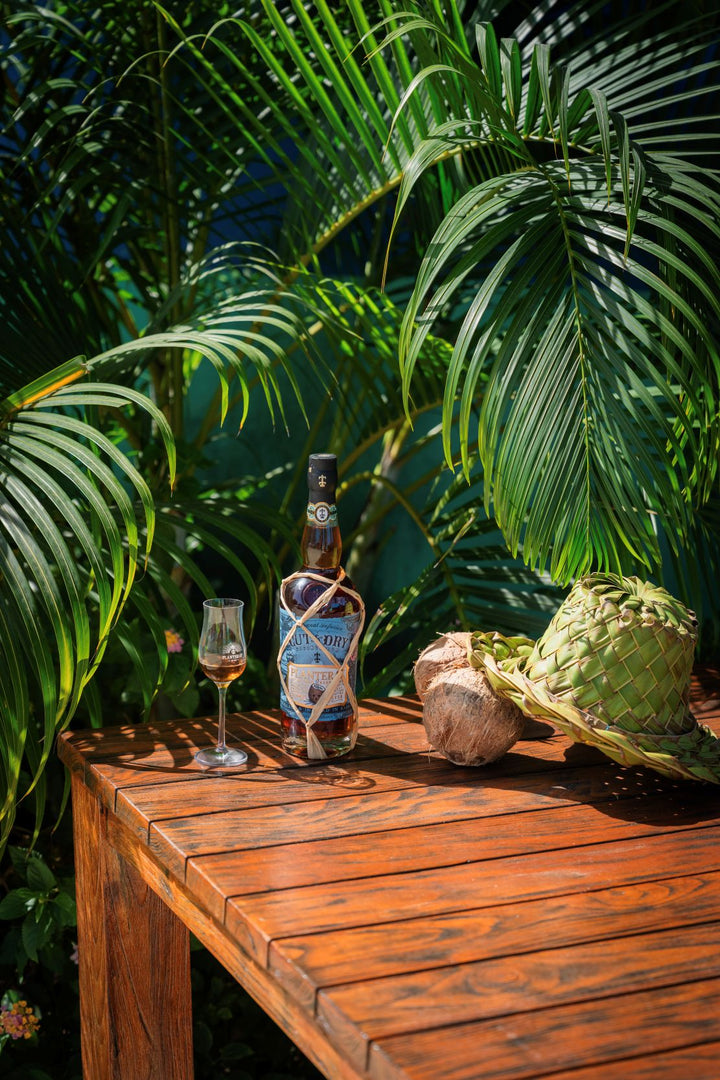 Bottle of rum and glass on a wooden table with tropical plants in the background