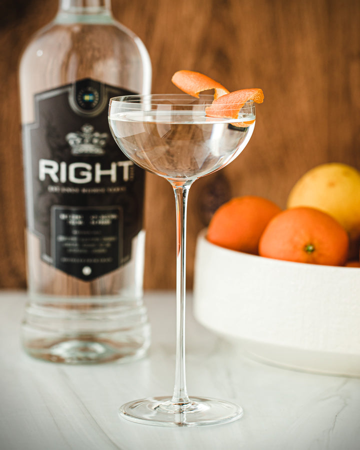 Cocktail glass with a bottle of 'Right' gin and oranges on a marble surface.