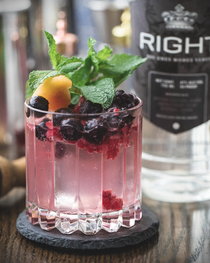 Pink cocktail with berries and mint leaves in a glass, accompanied by a bottle labeled 'Right'