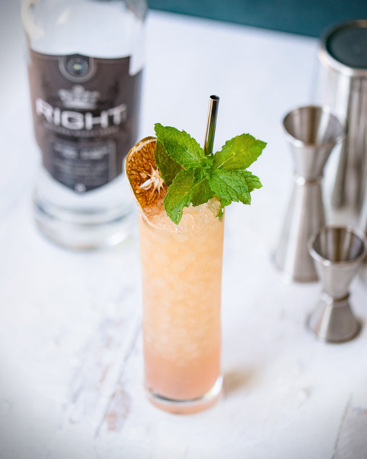 Cocktail with garnish next to a bottle of 'The Right' gin on a white surface.