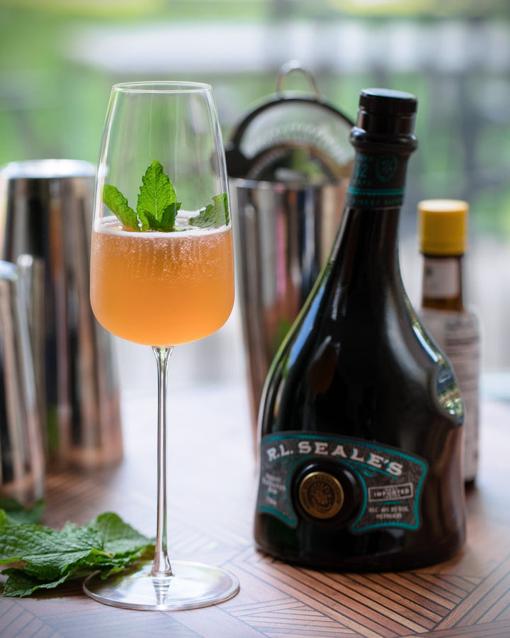 Alcohol bottle with a cocktail in a glass garnished with mint leaves on a wooden surface.