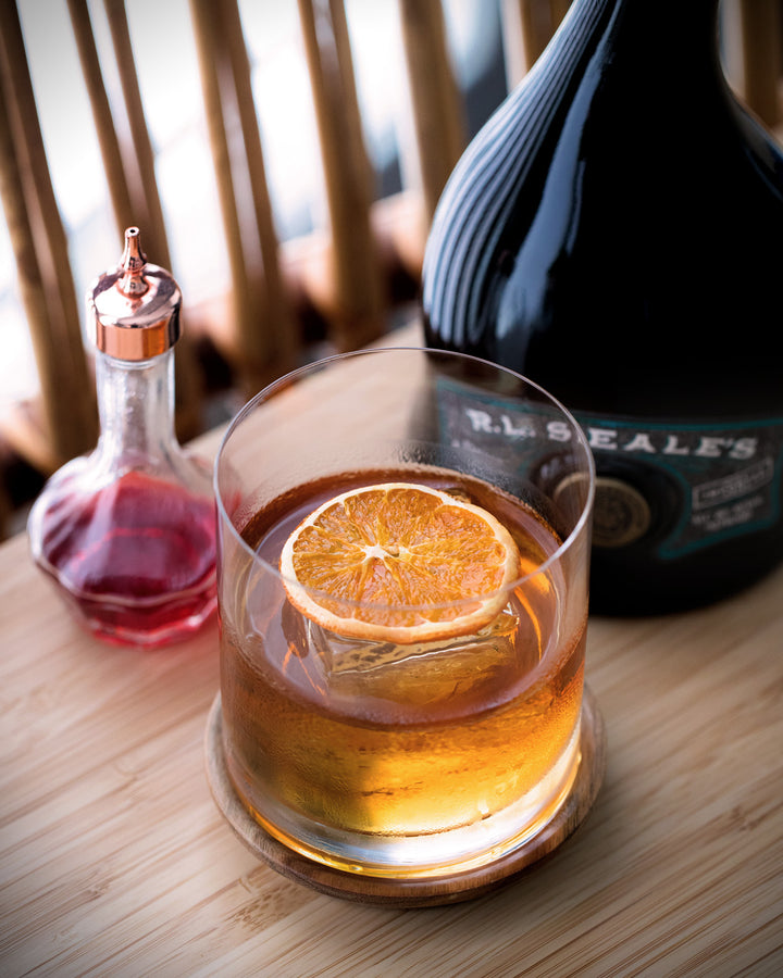 Glass of whiskey with an orange slice, bottle of R.L. Peale's in the background