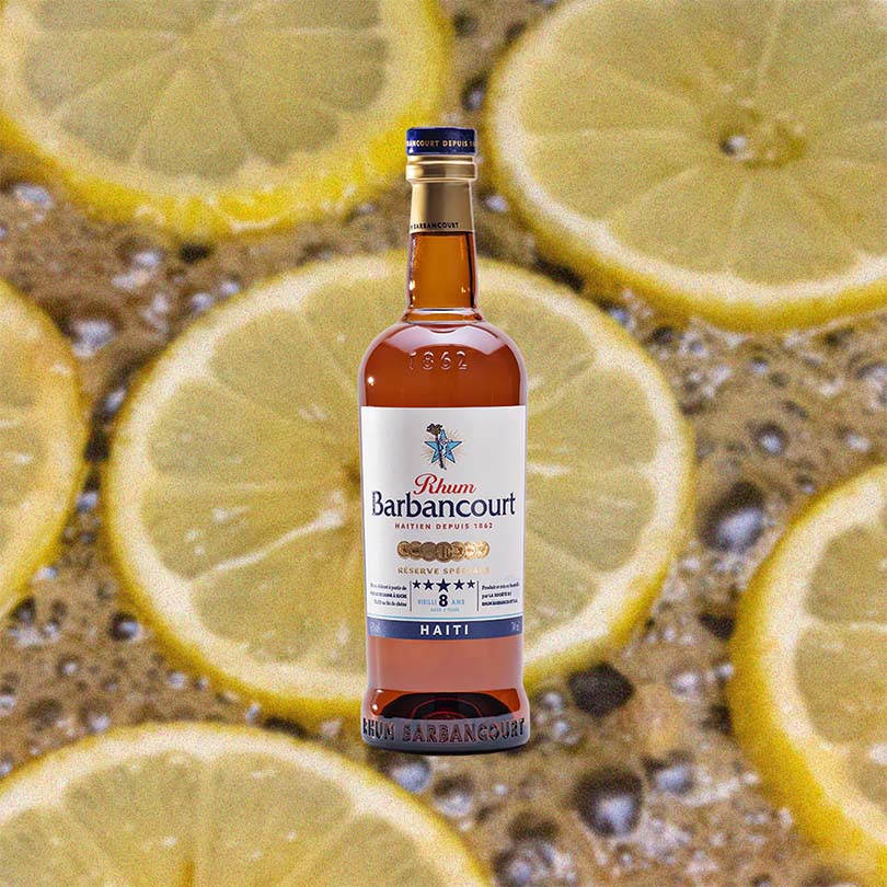 Bottle of Rhum Barbancourt 5 Star 8 Year Old Rum over backdrop image of sliced lemons floating in liquid.