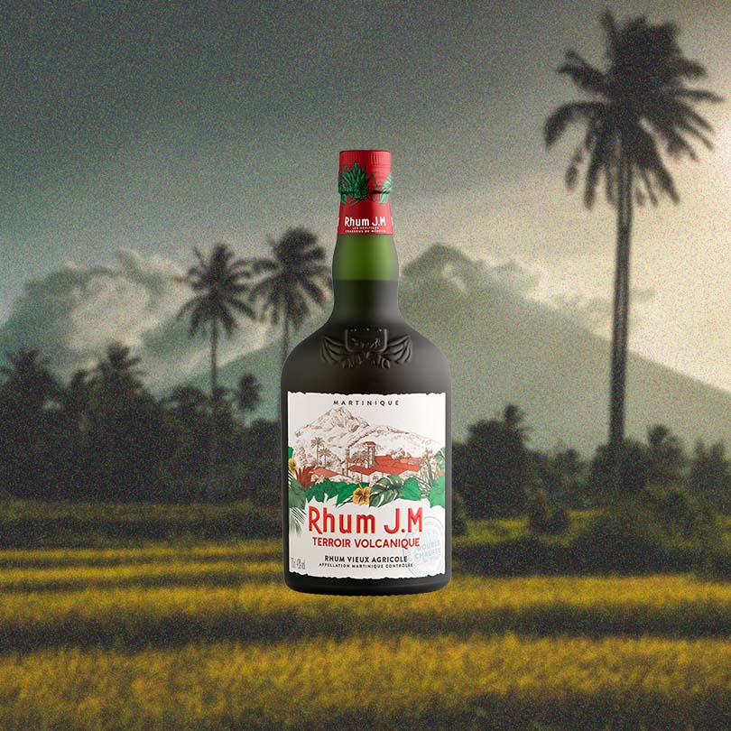 Bottle of Rhum J.M Terroir Volcanique Rum over backdrop image of a mountain and palm tree.