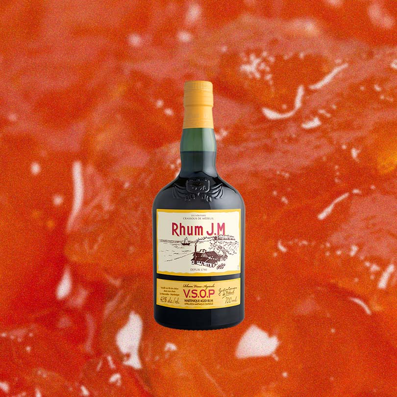 Bottle of Rhum J.M VSOP Martinique Aged Rum over backdrop image of orange, red gel.