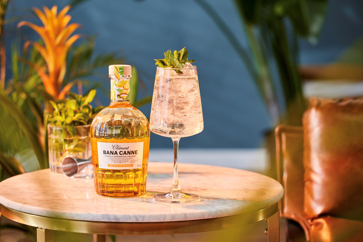 Bana Canne bottle and glass with a drink on a table with plants in the background