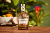 Bottle of Mahina Coco rum on a wooden surface with tropical fruits and plants in the background