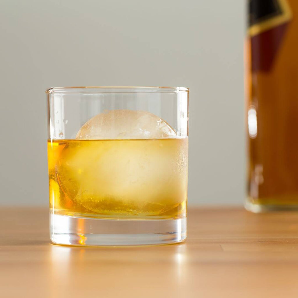 Upclose photo of a rum old fashioned cocktail on a table with large ice cube. 
