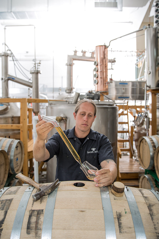 Person sampling from a barrel in a distillery setting