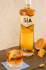 Bottle of SIA scotch whisky with a glass of whisky and orange slices on a wooden surface.