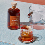 A bottle of Starward (New) Old Fashioned Whisky Cocktail to the left, an ice bucket in the background, and a delicious looking Old Fashioned in the foreground. The colors are light blue and orange, and the feel is distinctively neo-retro.