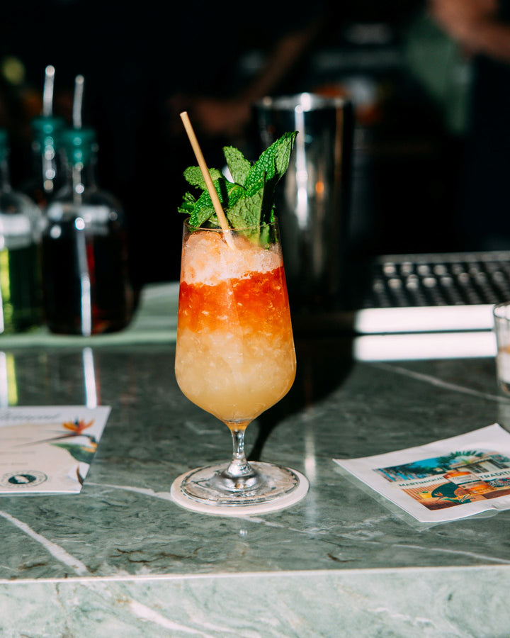 Layered cocktail with a straw and mint leaf on a bar counter