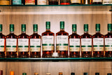 Row of Clement brand bottles on a wooden shelf with various other bottles in the background.