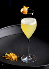 Cocktail in a glass with a frothy top and orange zest on a black background