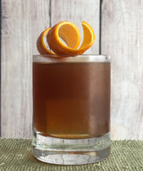 Brown cocktail in a glass with orange garnish on a wooden surface